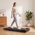 Woman in loungewear walking on the Belva under desk walking pad treadmill in a living room